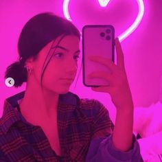 a woman taking a selfie in front of a neon heart