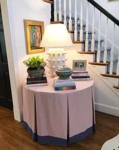 there is a table with books on it and a lamp next to the stair case