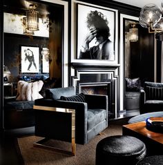 a living room filled with black furniture and pictures on the wall above it's fireplace