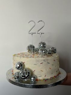 a birthday cake with silver decorations and two candles on top is being held by a person