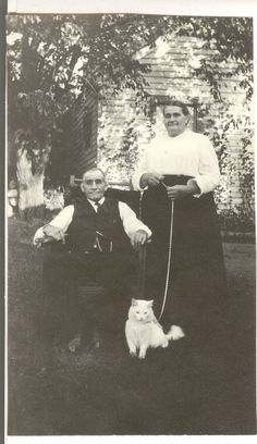 an old black and white photo of two people with a dog on a leash in front of a house