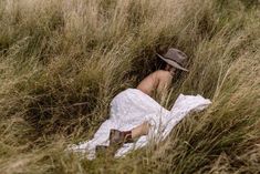 a woman in a white dress and hat is sitting in tall grass with her back to the camera