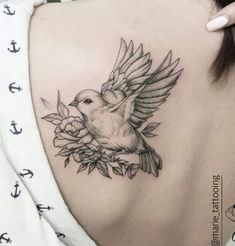 the back of a woman's shoulder with a bird and flowers tattoo on it