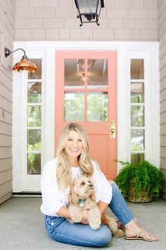 a woman sitting on the ground with her dog in front of a door and potted plant