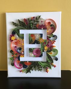 a white frame with colorful paper flowers and leaves in the shape of a letter e