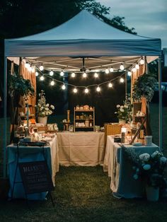 an outdoor tent with lights strung from the ceiling and tables covered in linens under them