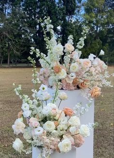 an arrangement of white and peach flowers in a box on the grass with trees in the background