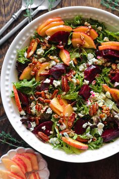 a white bowl filled with salad and sliced apples on top of a wooden table next to utensils