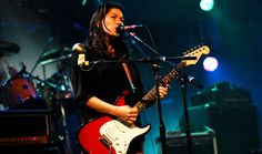 a woman singing into a microphone while playing an electric guitar