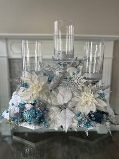 a centerpiece with white and blue flowers on top of a glass table in front of a fireplace