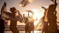 some people are dancing on the beach at sunset