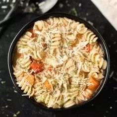 a black bowl filled with pasta and vegetables on top of a table next to a spoon