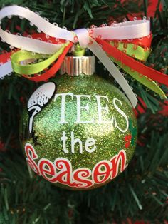 a green ornament hanging from a christmas tree with red, white and green ribbon