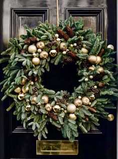 a christmas wreath on the front door with gold ornaments and pine cones hanging from it