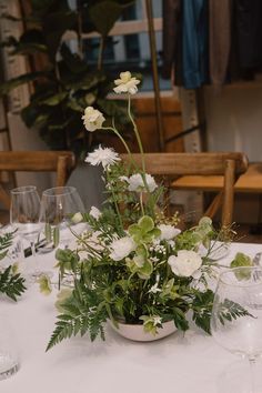 a white table topped with lots of flowers and greenery next to empty wine glasses