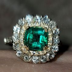 an emerald and diamond ring on someone's hand