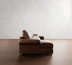 a brown leather couch sitting on top of a wooden floor next to a white wall