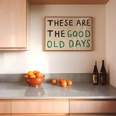 there are some oranges on the counter next to a bowl and bottle in the kitchen