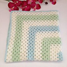 a crocheted square sitting on top of a white table next to pink flowers