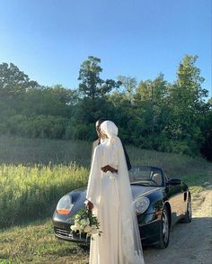 a bride and groom standing in front of a car on the side of the road