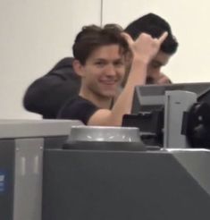 two people sitting at an airport with their hands in the air and one person standing behind them