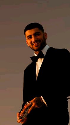 a man in a tuxedo is smiling at the camera while holding his cell phone