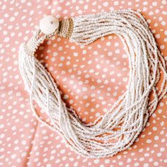 a white heart shaped necklace on top of a pink polka dot blanket with pearls and beads