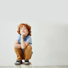 a little boy sitting on top of a white floor with his hands under his chin