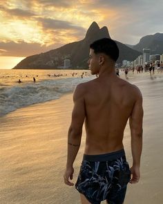 a man standing on top of a sandy beach next to the ocean with people in the background