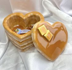 a heart shaped box with a golden bow on it sitting on a white cloth covered tablecloth