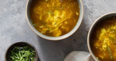 two bowls filled with soup on top of a gray counter next to some green vegetables