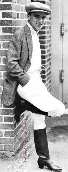 an old black and white photo of a man leaning against a brick wall with his hat on