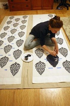 a woman sitting on the floor working on an area rug with black and white designs