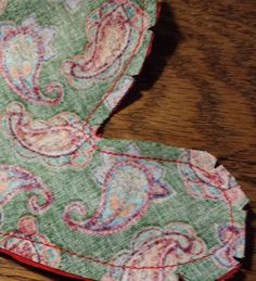 a green paisley tie with red trim on a wooden table next to a pair of scissors