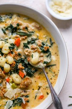 a bowl of soup with meat, vegetables and cheese in it next to a spoon