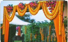 an outdoor wedding decorated with orange and pink flowers, garlands and yellow draping