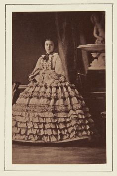 an old black and white photo of a woman wearing a dress with ruffles