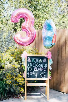 an outdoor welcome sign with balloons and streamers in the shape of the number three