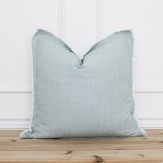 a light blue pillow sitting on top of a wooden floor next to a white wall