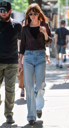 a woman walking down the street with a man in black shirt and jeans behind her