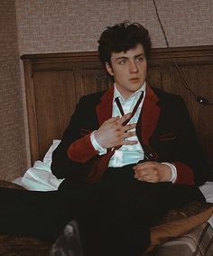 a man sitting on top of a bed wearing a red and black suit with white shirt