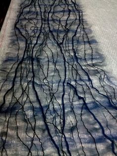 an artistically designed piece of fabric on a bed with blue and white sheets that have black branches growing out of it