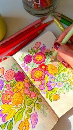 a person is drawing flowers on paper with colored pencils