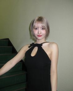 a woman in a black dress standing next to some stairs with her hand on her hip