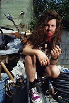 a man sitting on top of a pile of trash next to a guitar and other items