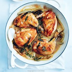 a pan filled with chicken and vegetables on top of a white tablecloth next to lemon wedges