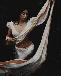 a woman is in the water wearing a white dress and holding a sheer fabric over her head