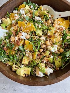 a salad with oranges, avocado, nuts and feta cheese in a wooden bowl