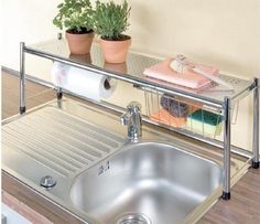 a stainless steel sink with two plants on the shelf above it and a towel rack