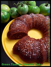 a cake on a yellow plate next to some green tomatoes and grapes with the words green tomato brownie cake